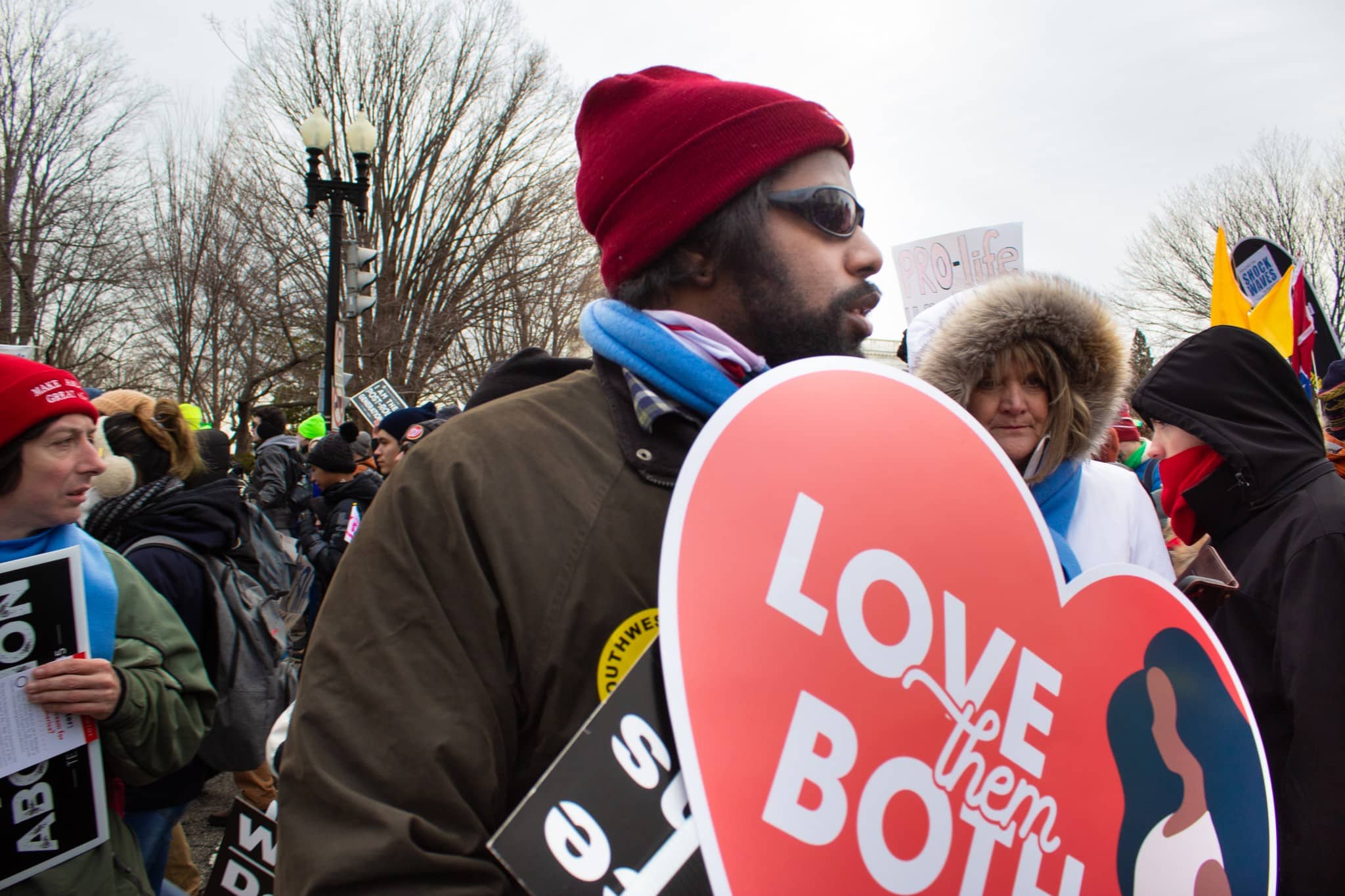 A man holds a sign saying “love them both” as he protests abortion and Roe v. Wade on January 21, 2022. (The American Spectator)