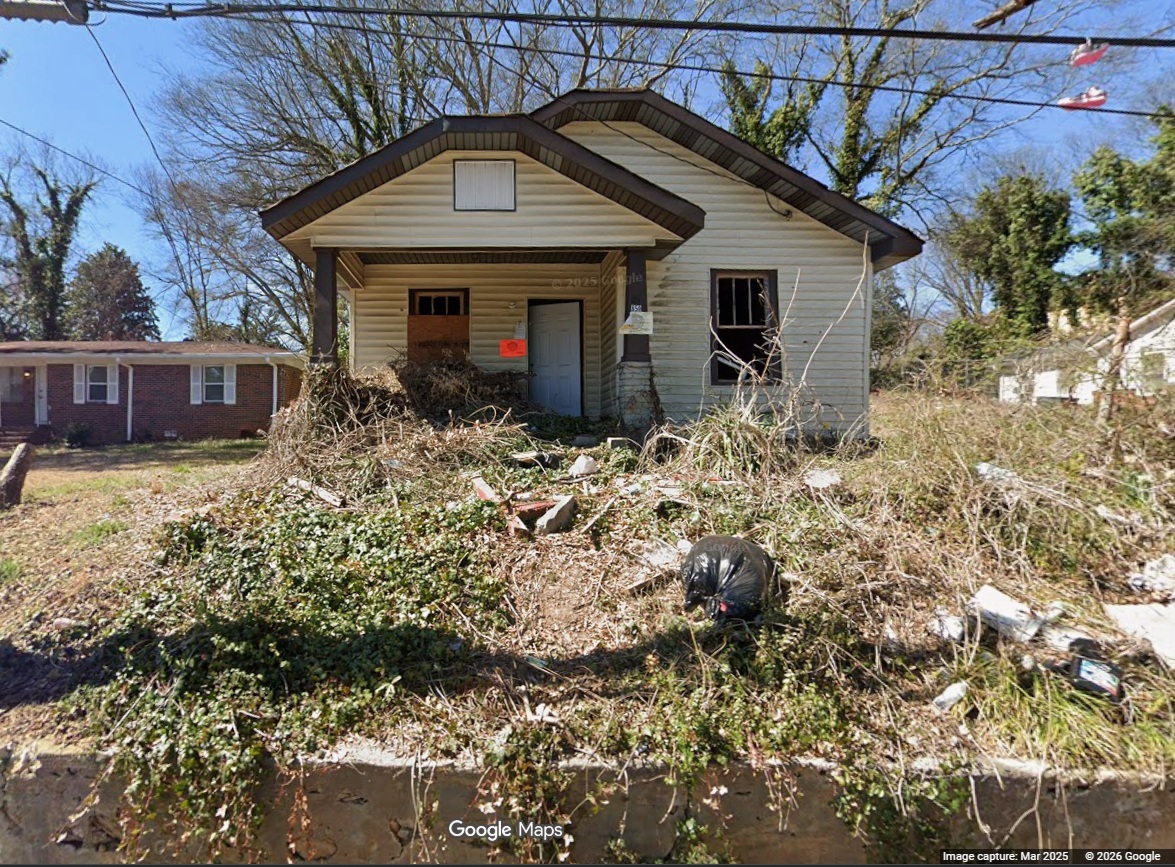 Overgrown and abandoned small house with a cluttered front yard.